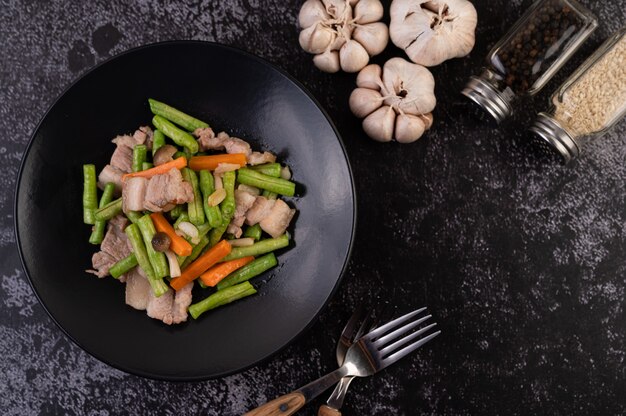 Stir-fried long beans and carrots, add pork belly, put on a black plate.