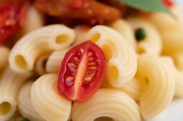 Stir-fried macaroni with tomato, chili, pepper seeds and basil in a white dish.