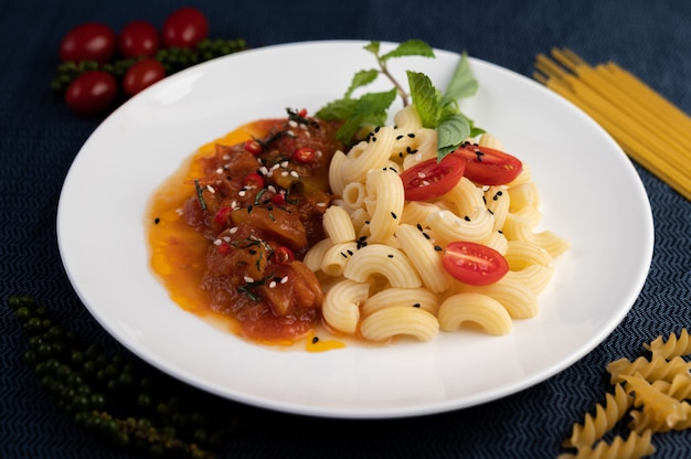 Foto gratuita maccheroni in padella con pomodoro, peperoncino, semi di pepe e basilico in un piatto bianco.