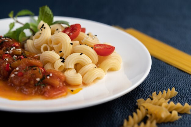 Жареные макароны с помидорами, перцем чили, перцем и базиликом в белом блюде.