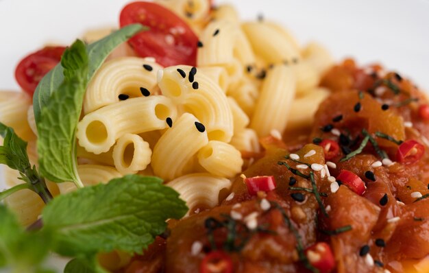 Stir-fried macaroni with tomato, chili, pepper seeds and basil in a white dish.