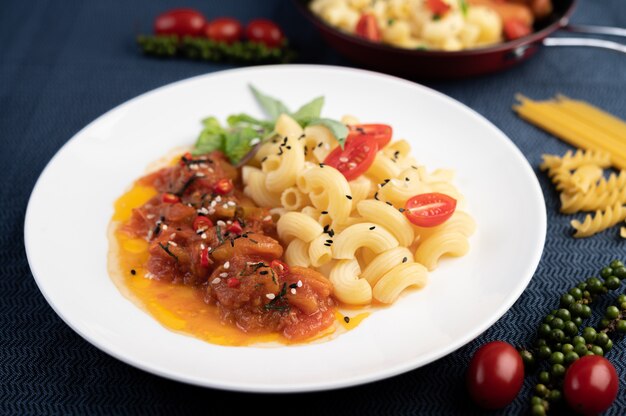 Stir-fried macaroni with tomato, chili, pepper seeds and basil in a white dish.