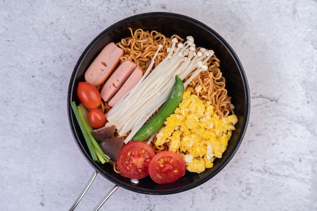 Free photo stir fried noodle that combines corn, golden needle mushroom, tomato, sausage, edamame and spring onions in a frying pan.