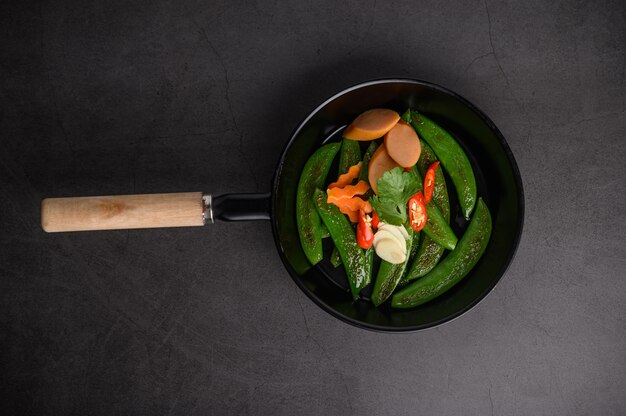 Stir-fried peas in a frying pan on black cement surface.