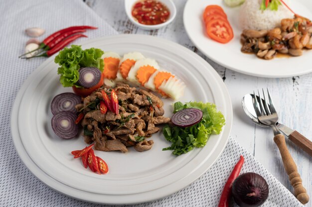 Stir fried pork basil on a white plate with carrots, Cucumber and Onion.