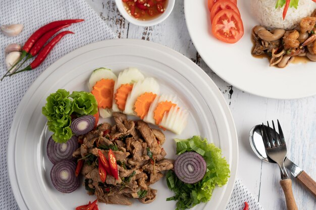 Stir fried pork basil on a white plate with carrots, Cucumber and Onion.