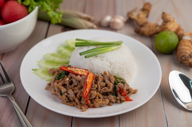 Stir fried pork with basil, fried egg in a white dish .