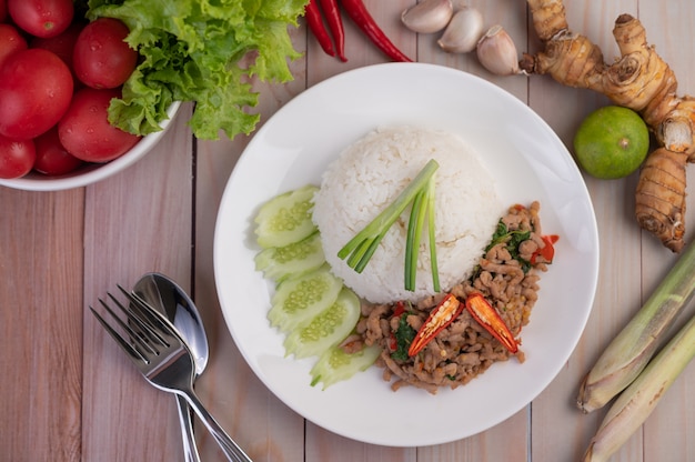 Stir fried pork with basil, fried egg in a white dish .