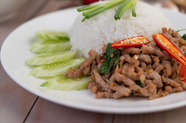 Stir fried pork with basil, fried egg in a white dish .