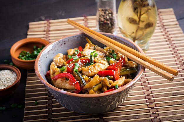 Stir fry chicken, zucchini, sweet peppers and green onion with chopsticks