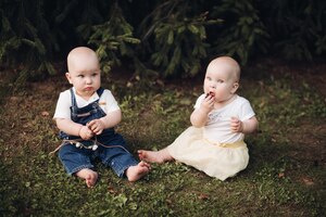 Free photo stock photo of adorable little babies sitting on the grass in the forest. little brother and sister eating berries while sitting on green grass in the forest.