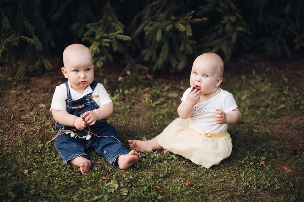 Stock photo of adorable little babies sitting on the grass in the forest. Little brother and sister eating berries while sitting on green grass in the forest.