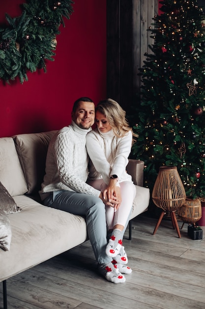 Stock photo of beautiful caucasian couple in xmas socks embracing on sofa next to christmas tree.