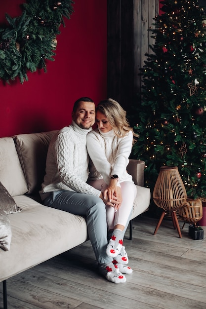 Stock photo of beautiful Caucasian couple in xmas socks embracing on sofa next to Christmas tree.