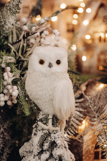 Stock photo of a beautiful toy owl of white color sitting on fir tree branch with bokeh lights in the background.