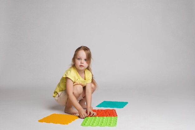 Сток-фото ребенка, играющего с красочными яркими резиновыми подушечками для улучшения и развития мелкой моторики на полу. Она сидит на корточках в студии.