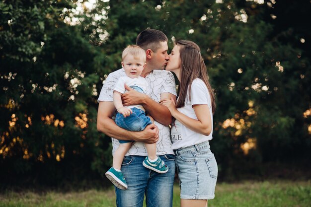 Stock photo portrait of kissing parents with a baby boy looking at camera. Little boy sitting on father s arm and looking at camera while his parents kissing.