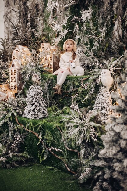 Stock photo. of pretty little girl in white dress and earmuffs looking up waiting for miracle while sitting in beautiful decorations with white toy rabbit.