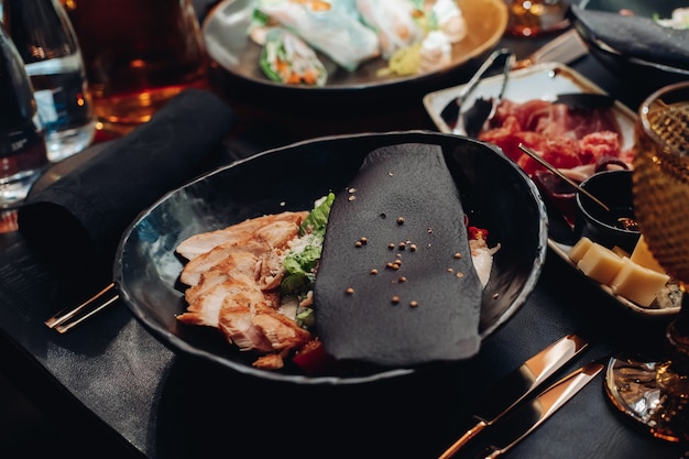 Stock photo of served nutritious Caesar salad with chicken served with black slice with sesame seeds on top.