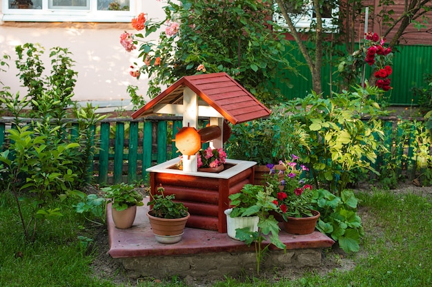 Stock photo of a small garden in the backyard. Fake well with potted flowers.