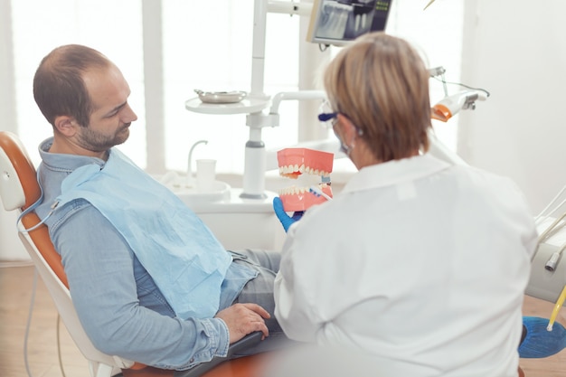 Стоматолог держит санитарную модель нижней челюсти, разговаривает с больным человеком
