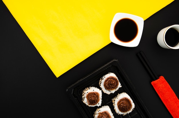 Foto gratuita piatto di pietra con rotoli di sushi su uno sfondo nero con ciotola di salsa di soia su sfondo giallo