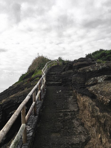 雨上がりの灰色の曇り空の下で木製の手すりが丘の頂上に向かって石の階段