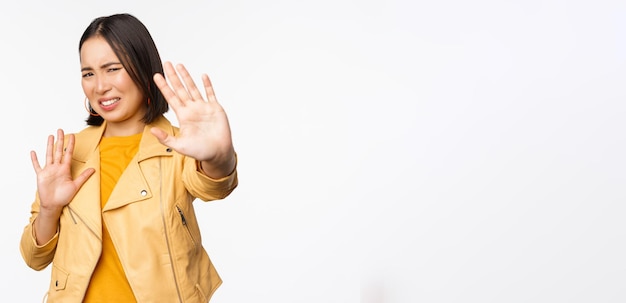 Stop get away from me back off concept Young disgusted asian woman being blinded by smth stretching out hands in defense blocking light standing over white background