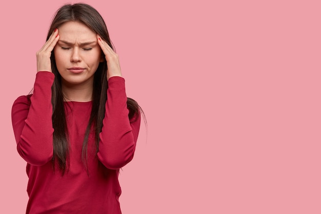 Stop my head blow out. Tired brunette young Caucasian woman keeps hands on temples, closes eyes