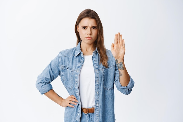 Foto gratuita fermati e esci donna accigliata seria che alza la mano per bloccare e mostra che non è d'accordo dicendo di no con la faccia sicura in piedi su uno sfondo bianco