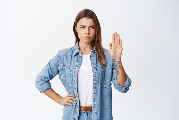 Stop and quit it Serious frowning woman raising hand to block and show she disagree saying no with confident face standing against white background