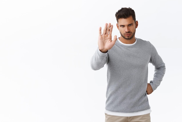 Stop right here Guy saying no seriously staring camera from under forehead raise hand in prohibition dont or forbid gesture give warning and disapproval of action standing white background