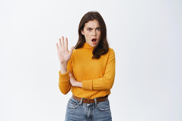 Stop right now Offended and shocked woman showing block gesture telling no frowning and looking insulted with disgusting offer refusing standing against white background