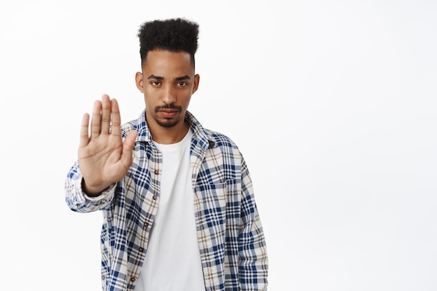 Free photo stop. serious and determined african american guy extend palm, saying no, rejecting and prohibit smth, stay away, keep social distancing, standing over white background