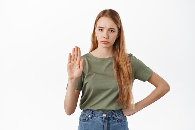 Stop she says no Serious displeased woman showing raised palm to block disapprove something prohibit and reject standing against white background Copy space