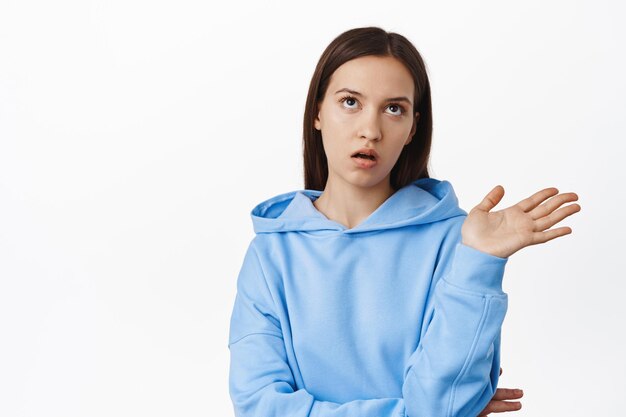 Stop talking. Annoyed young arrogant woman do eye roll, wave away, telling to quit speaking, bored with conversation, standing in hoodie against white background