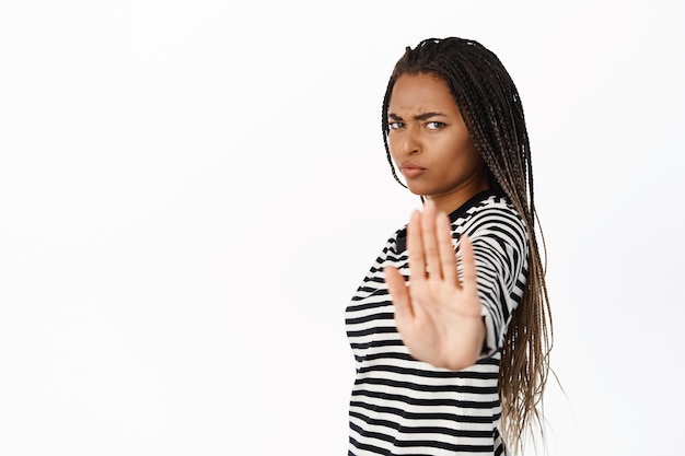 Бесплатное фото Остановите эту серьезную африканскую женщину, протягивающую руку в камеру, показывающую запретный жест ладони, переставая говорить, что нельзя стоять на белом фоне