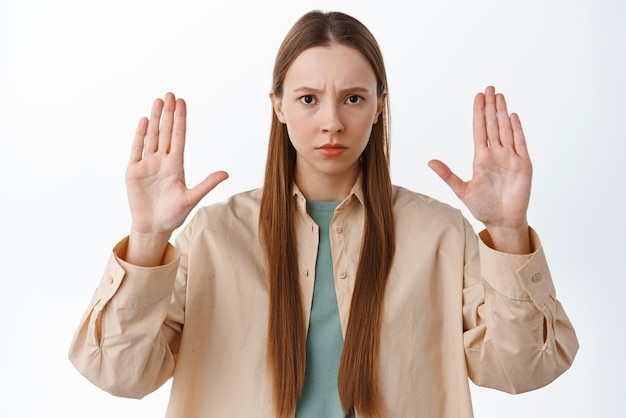 Free photo stop this stay away keep distance serious frowning girl showing block gesture say no raise hands to prohibit forbid something refusing standing over white background