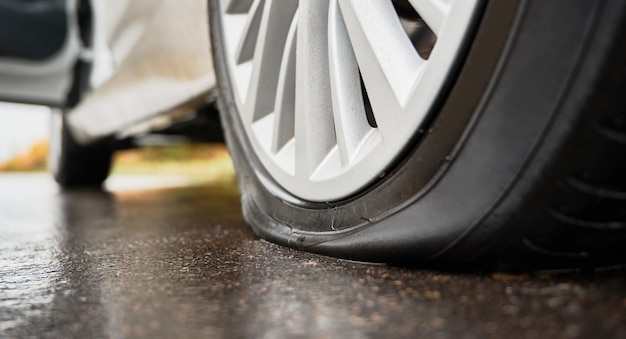 Stopped white car with punctured tire on roadside