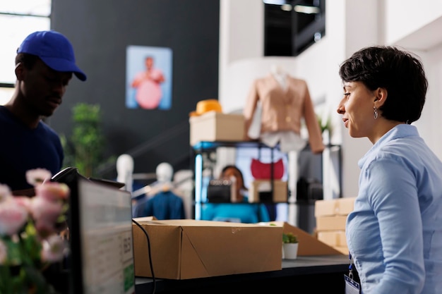 Free photo store manager talking about delivery with courier, preparing packages in modern boutique. employee standing at counter desk, working with online order, checking logistics report on computer.