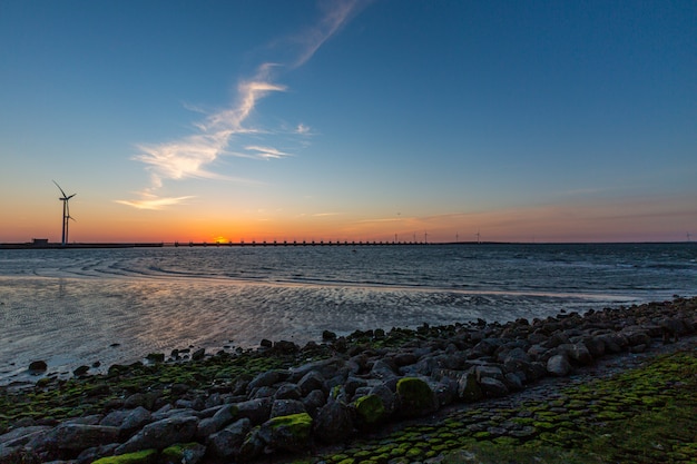 A storm surge barrier and windmills in Zeeland province in the Netherlands on sunset