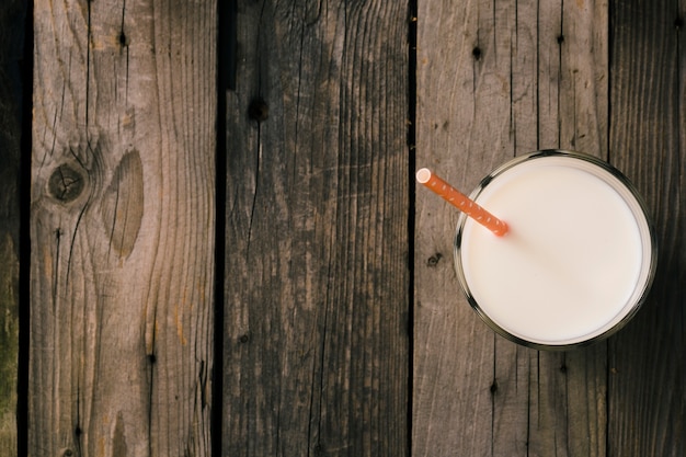 Straw in the glass of milk over the rustic wooden background