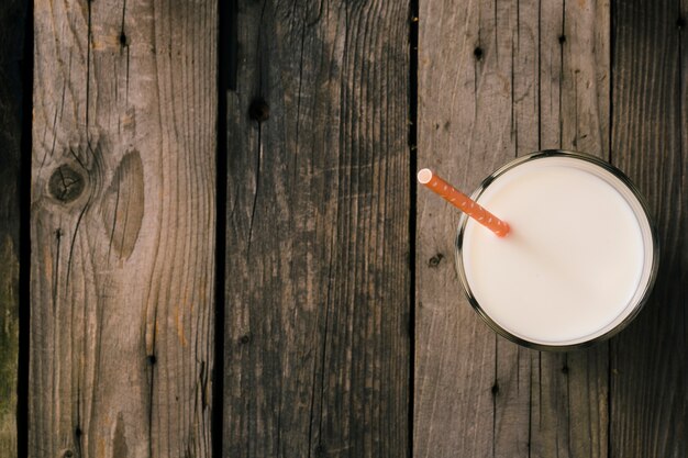 Straw in the glass of milk over the rustic wooden background