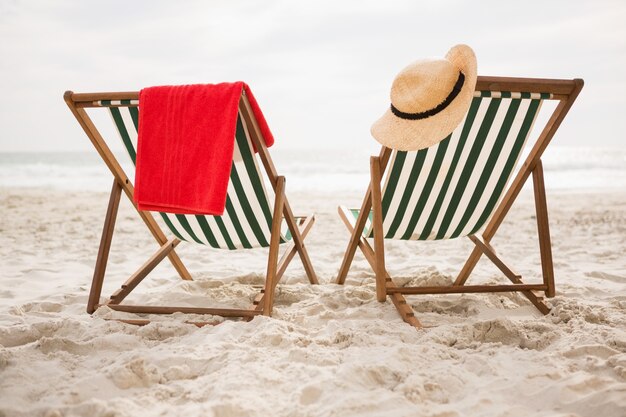 Straw hat and towel kept on beach chairs