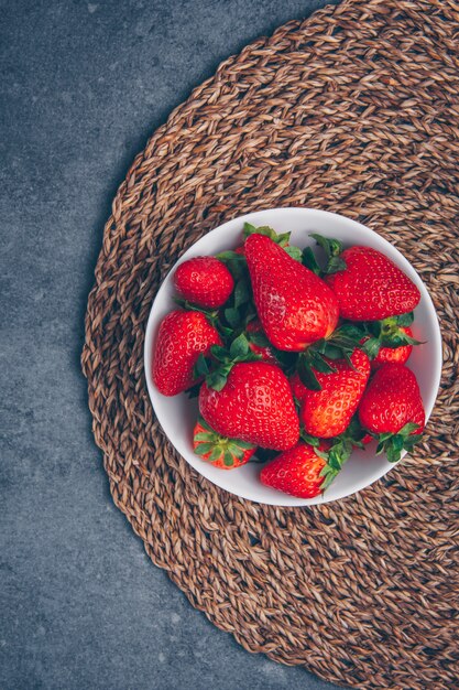 Strawberries in a bowl on a trivet and gray textured background. top view.