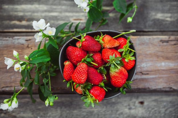 Strawberries in a bowl with flower branch top view on old wooden table