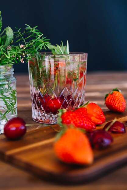 Strawberries and cherries on chopping board in front of juice with ingredients