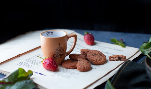 Strawberries, cookies and coffee cup on a book paper. 