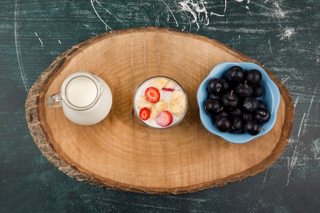 Strawberries in cream served with milk and cherries on a wooden platter, top view