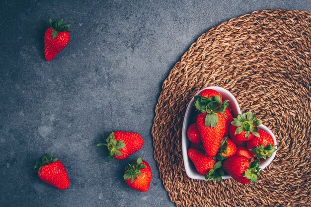 Strawberries in a heart shaped bowl on a trivet and gray textured background. top view. free space for your text